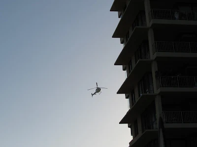 Helicopters hover near building at sunset