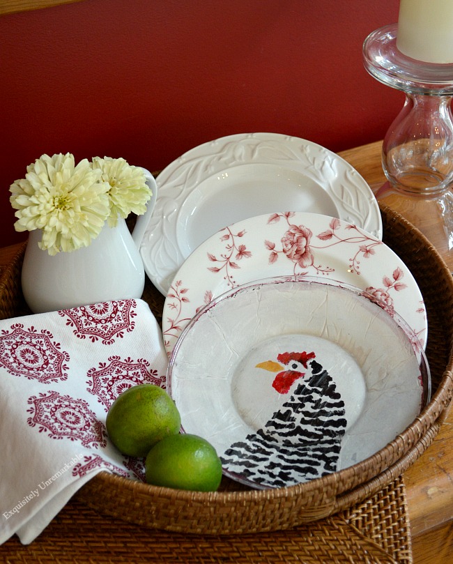 Custom stenciled glass plate with chicken head sitting in a basket with other plates