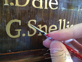Close up photograph of a paintbrush being held painting the free hand letters for the honours board.