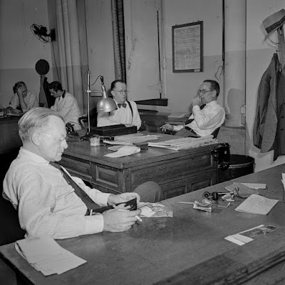 In the bullpen. The assistant managing editor sits in the foreground while the managing editor and night managing editor confer in the background.