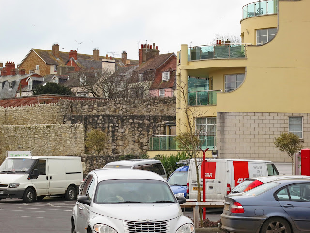 Cars, vans, houses and flats and ruins of old walls.