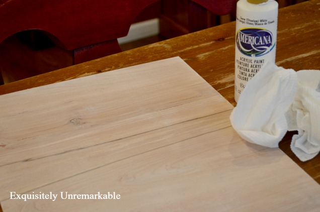 White washing a wooden board with paint to make a wooden sign