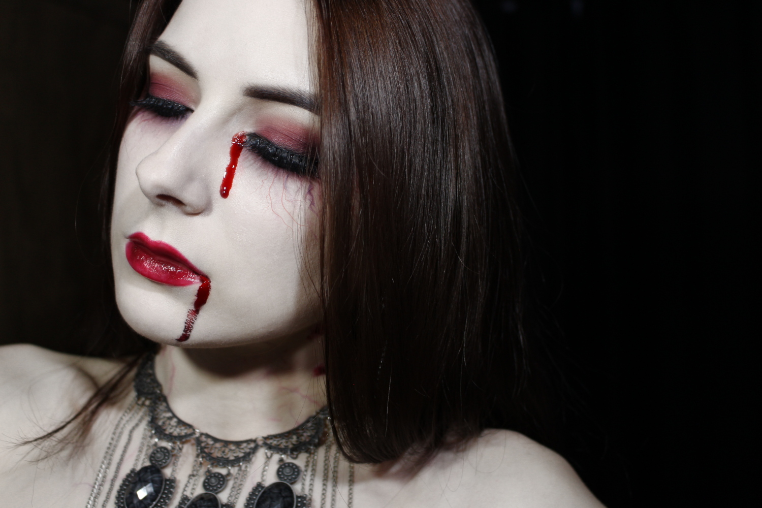 a close-up of Liz Breygel's face with a dramatic vampire makeup look and false blood tears for Halloween.