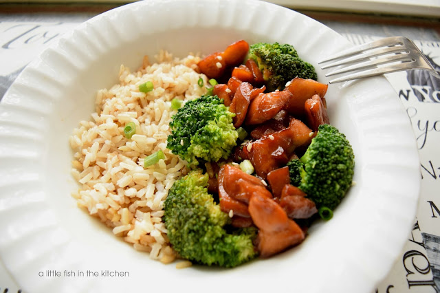 A white bowl is filled with cooked rice, steamed broccoli and pieces of Teriyaki chicken. A fork leans on the side of of the bowl. 