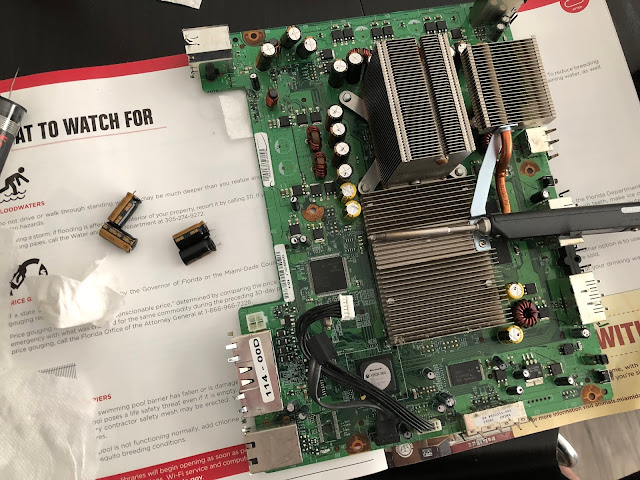an Xbox 360 main board, with a soldering iron on top of it and several capacitors next to it