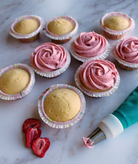 vanilla cupcakes getting strawberry buttercream piped on