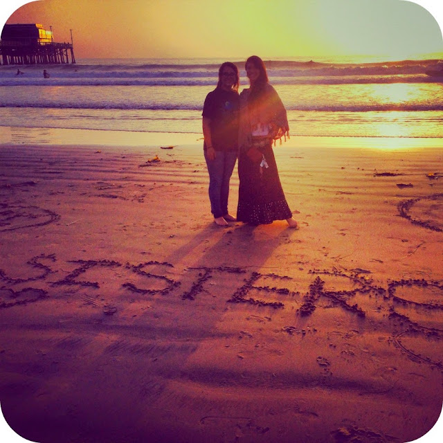 Two girls by the ocean writing Sisters in the sand