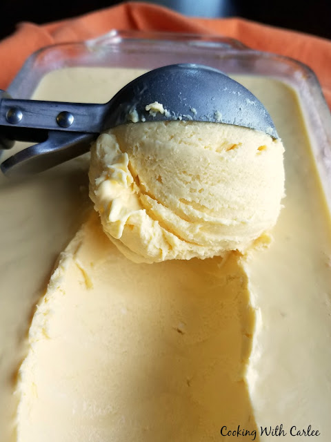 Super creamy homemade orange creamsicle cheesecake ice cream is going to be a new summer favorite dessert. It is cold, refreshing and has the perfect combination of orange and vanilla with a cream cheese twist! scoop of ice cream being scooped out of loaf pan