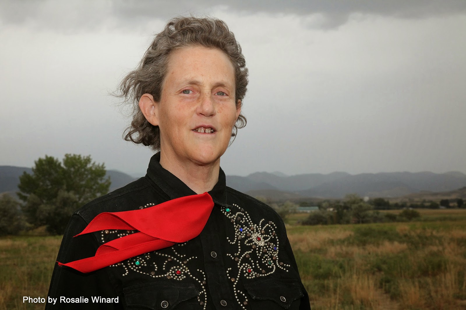 Usmívající se Temple Grandin s černou vyšívanou košilí a červeným šátkem