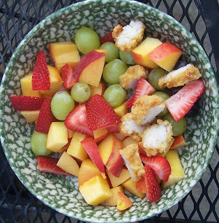 fried chicken tenders cut up in bowl of cut up peaches, cut up strawberries, and white grapes