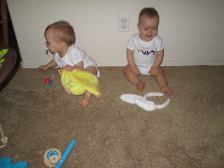 picture of twin baby girls sitting against a wall, one leaning away one laughing