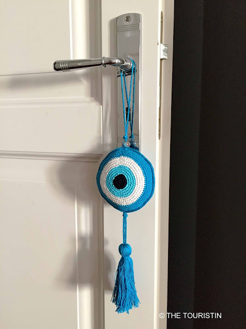 Knitted Evil Eye on a silver-coloured doorknob of a white wooden door.