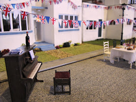 Miniature scene of a piano at a VE Day street party in front of a row of Art Deco houses.