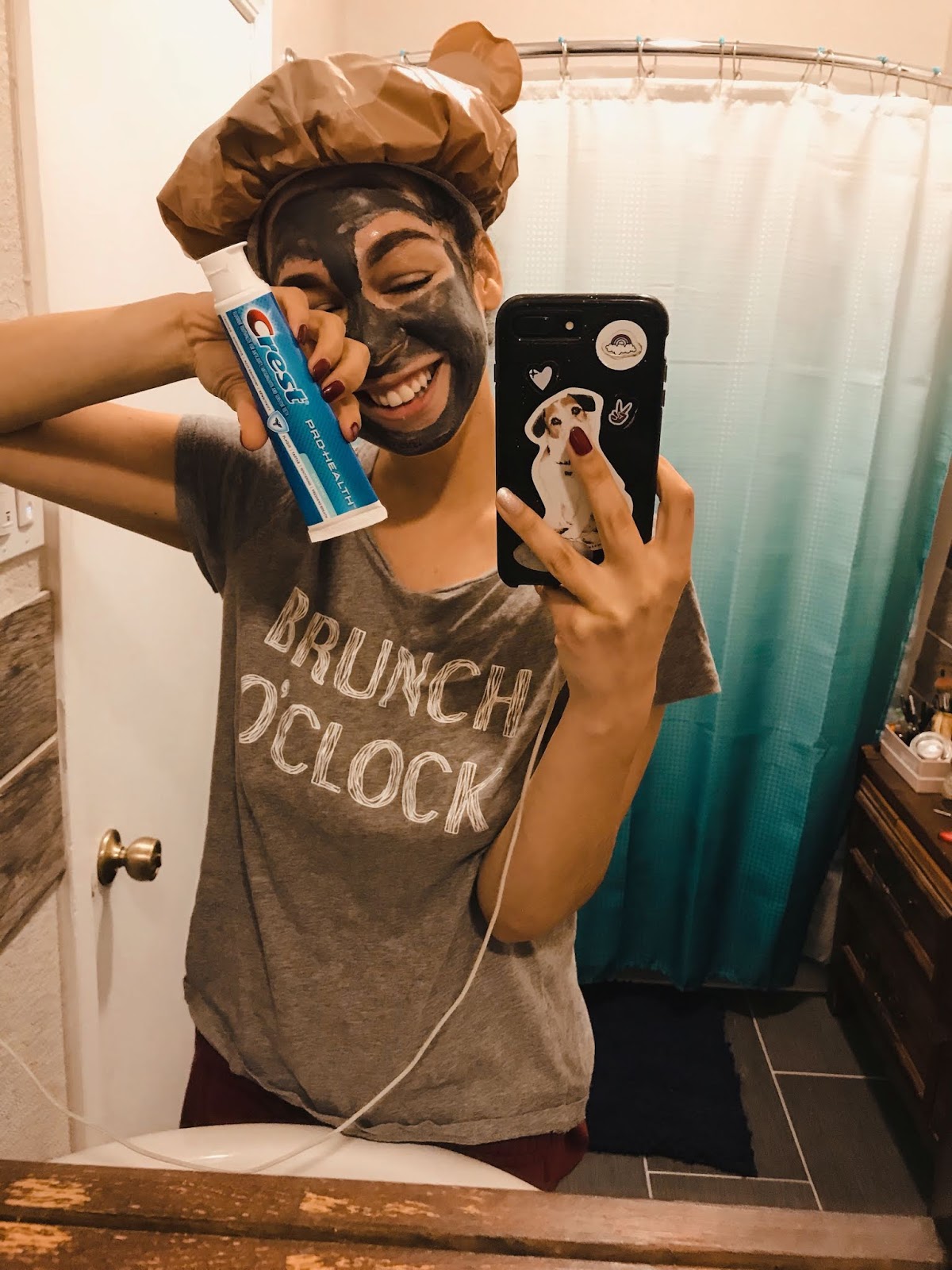 Amber "aMused Blog" taking mirror selfie. Wearing a grey clay mask, and holding crest toothpaste