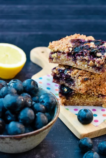 A stack of blueberry and lemon oaty bars with a few scattered blueberries