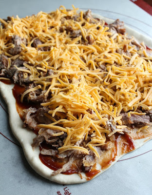 bread dough rolled out and topped with bbq sauce, pulled pork and shredded cheese