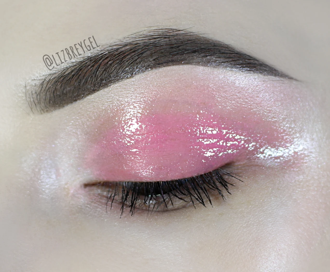 a close-up of an eye with a rose, glossy eye lid makeup look and well-defined eyebrow.