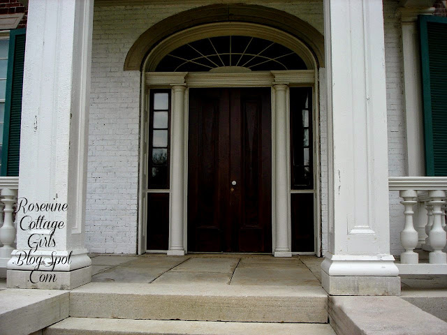 Photo of the front of the Carnton Plantation. The face of the house is white painted brick and the double doors and side lights to the right and left of the doors are painted black. The pillars are white as well as the railings. by Rosevinecottagegirls.com