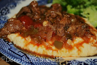Strips of round steak, slow stewed with tomatoes and vegetables and served over a bed of garlic cheese grits.