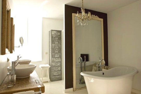 Bathroom in mansion with stand alone tub, chandelier, traditional mirror next to tub and bowl sinks