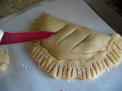 A close up photo of a knife making slits on the top of an unbaked cherry hand pie.