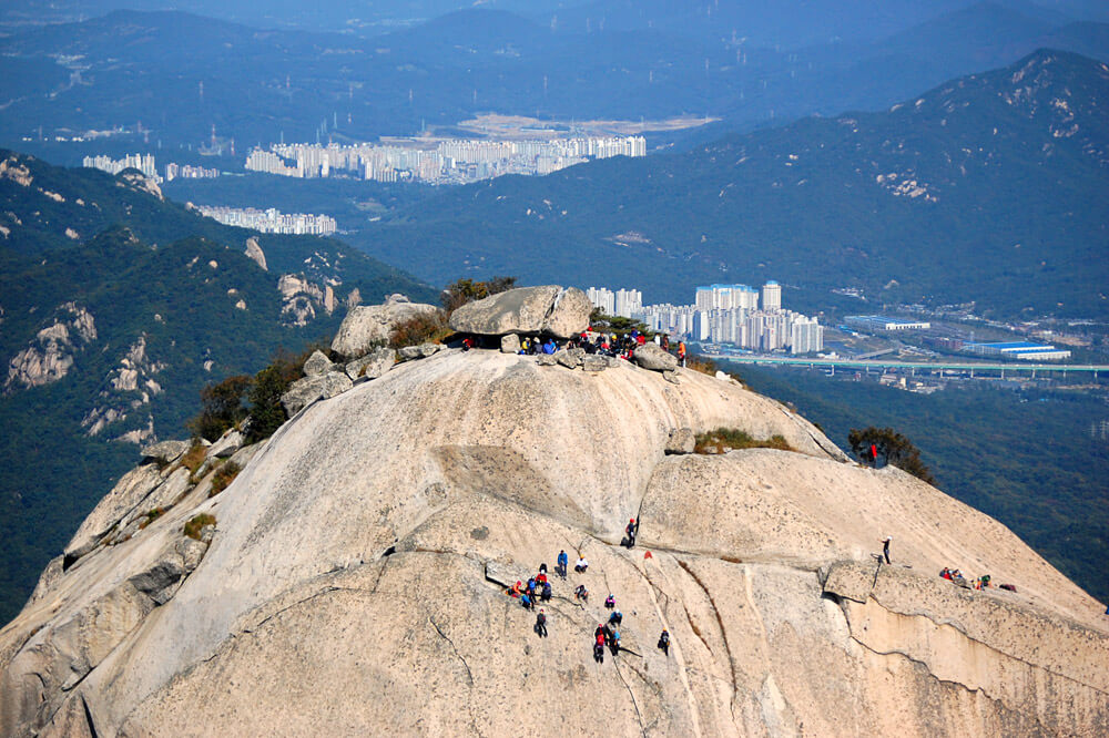 Hikers on a rock to the top with the city view background, The people look like ants on the side of the mountain view in the distance Insubong Peak, Mt. Bukhansan National Park. Best 10 Seoul Attractions | Explore Amazing Things to Do in Seoul