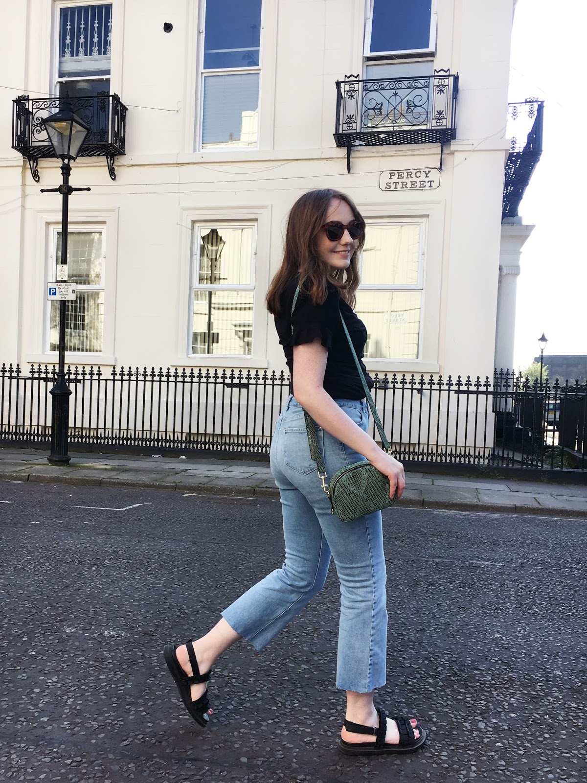 UK style blogger wearing black button up dress as top, light blue kick flare jeans and black sandals with green snake print cross body bag