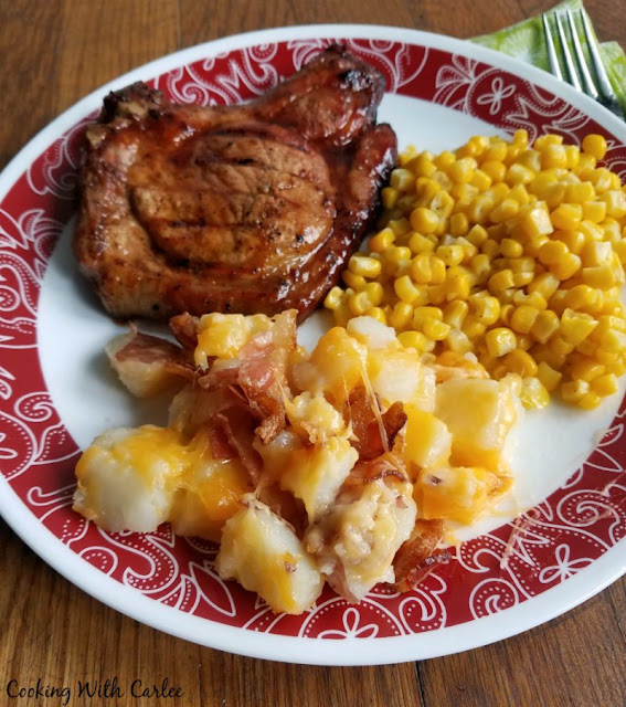 Loaded with cheese and bacon, these potatoes are going to disappear before you even know what happened! Great for BBQs, potlucks or family dinners! plate of BBQ pork chops, corn and potatoes with cheese and bacon