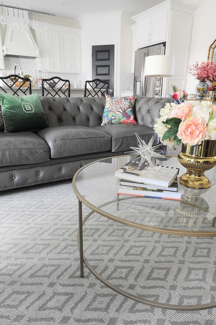 A glam and feminine living room with a gray chesterfield sofa, glass coffee table and a neutral rug by Karastan. A glam and feminine living room with a gray chesterfield sofa, glass coffee table and a neutral rug by Karastan.