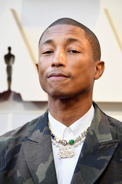 Pharrell sfoggia due collane: la prima in oro giallo con diamanti, zaffiri e smeraldi di taglio vario, la seconda di perle naturali con un centrale personalizzato con il suo nome impreziosito da diamanti.
