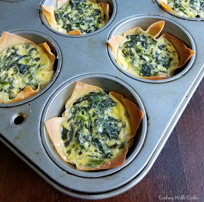Tiny little quiche are filled with spinach and cheese for a couple bite of brunch goodness. They are perfect for making ahead and heating and eating later! mini spinach and cheese quiche in golden wonton wrappers in cupcake tin fresh from oven