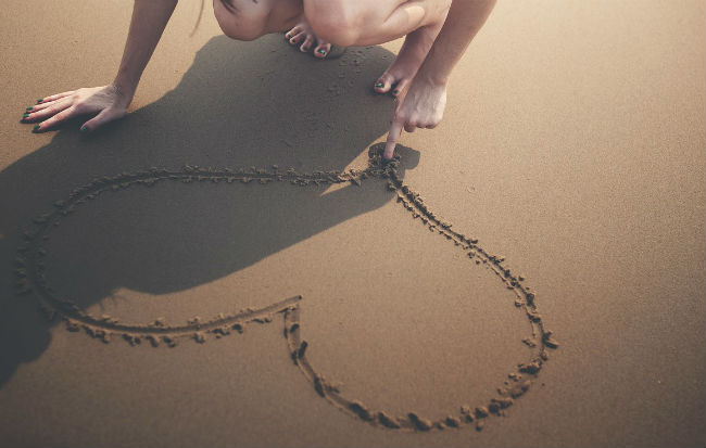 Donna che disegna un cuore sulla sabbia