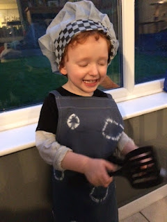 Very happy boy dressed as a chef holding a pan and spatula