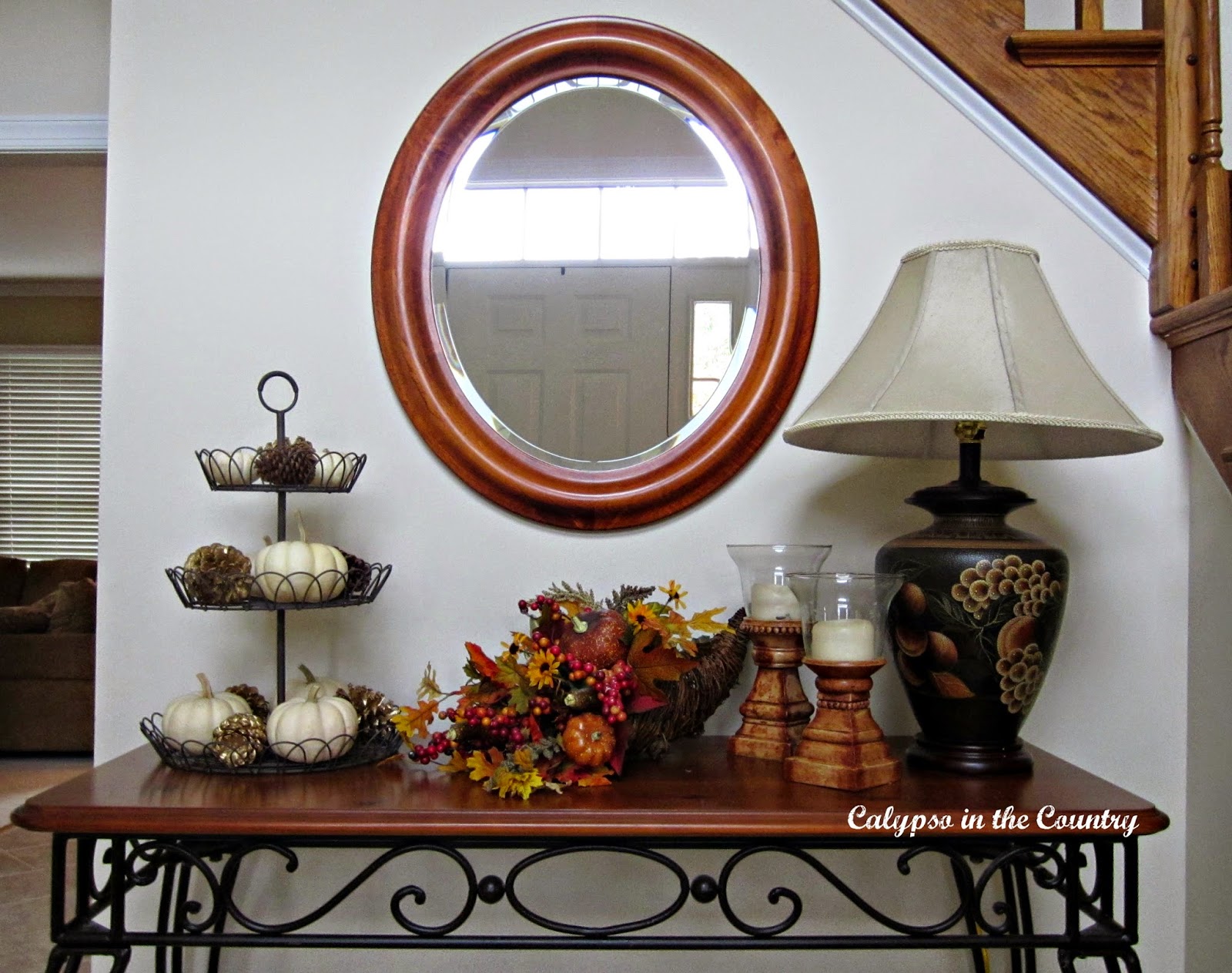 Foyer table decorated for fall with oval mirror above 