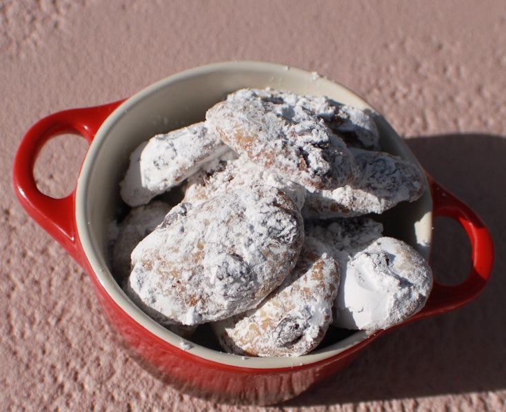 these are cookies in a red ceramic bowl for All Souls Day also All Saints Day cookies. The cookies are spiced and rolled in powdered sugar. This recipe is how to make traditional All Souls Day cookies.