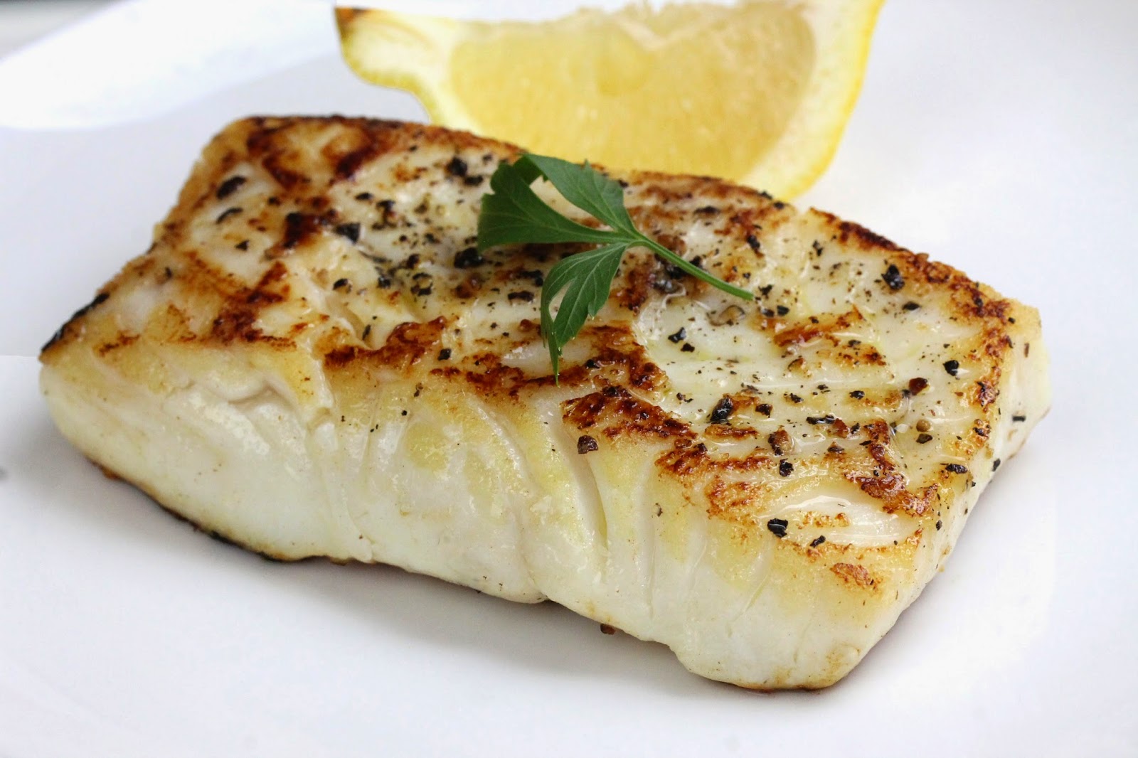 A pan seared fish filet, seasoned and ready to eat. Garnished with a parsley sprig and a lemon wedge.