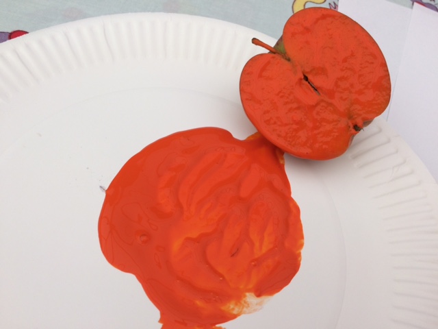 An apple cut in half, having been dipped in orange paint from a paper plate