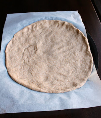 A round of pizza dough patted out and ready for toppings