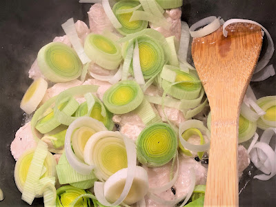 Partially cooked diced chicken breast and sliced leeks in a frying pan