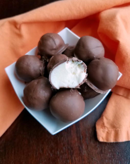 Bites of creamy orange cheesecake goodness are dipped in chocolate to make this one of a kind no bake treat! open bonbon with creamy center showing inside chocolate shell