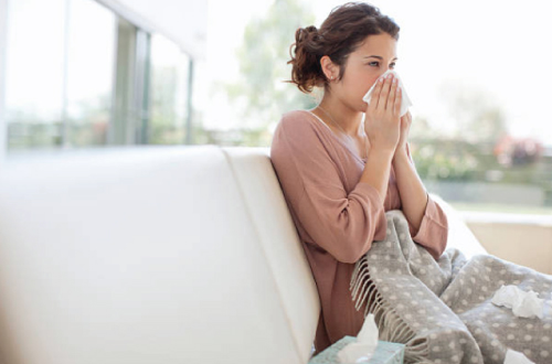 woman sitting on couch blowing nose