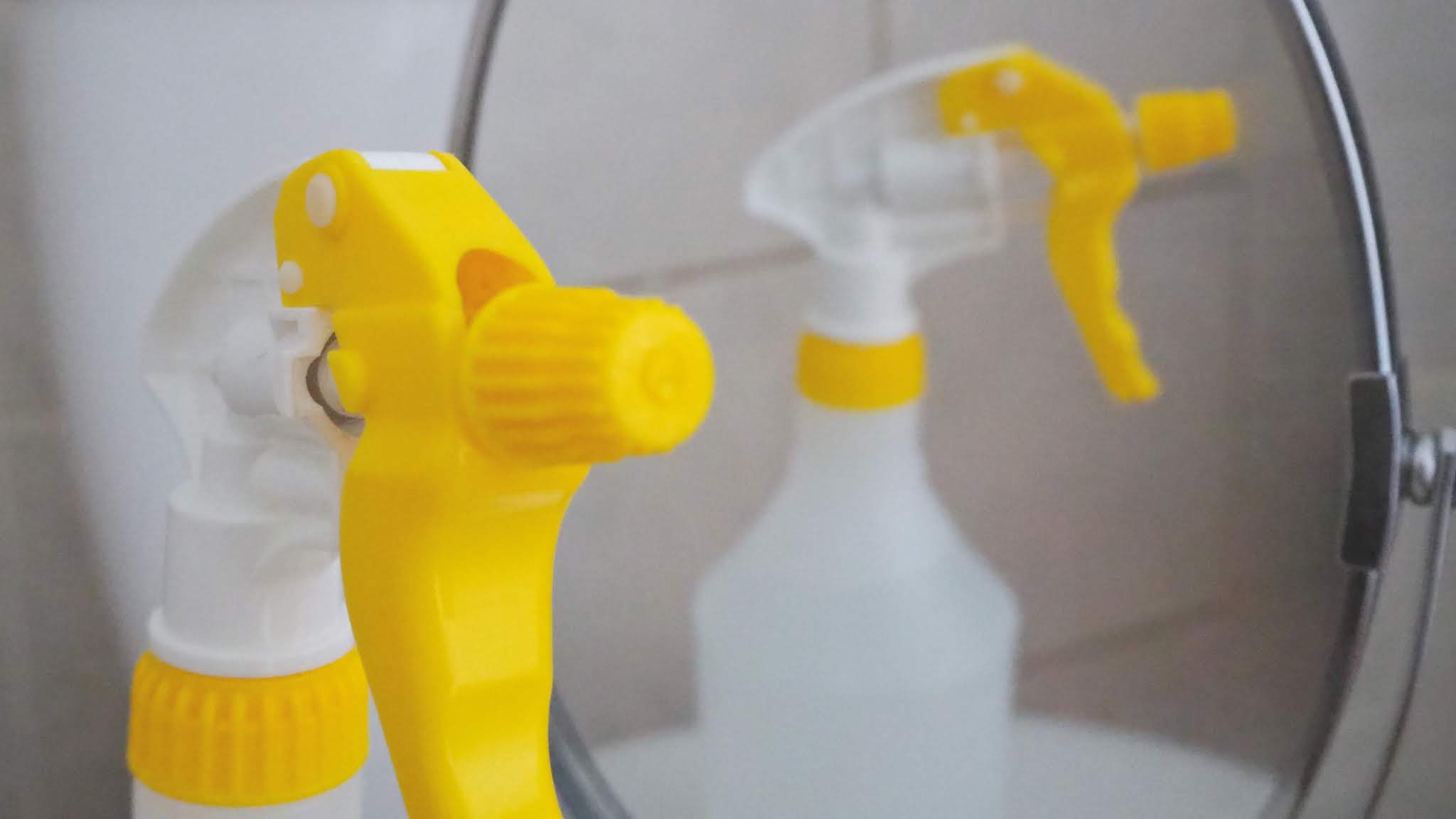 Yellow and white spray bottle in front of a mirror with homemade kitchen & glass cleaner