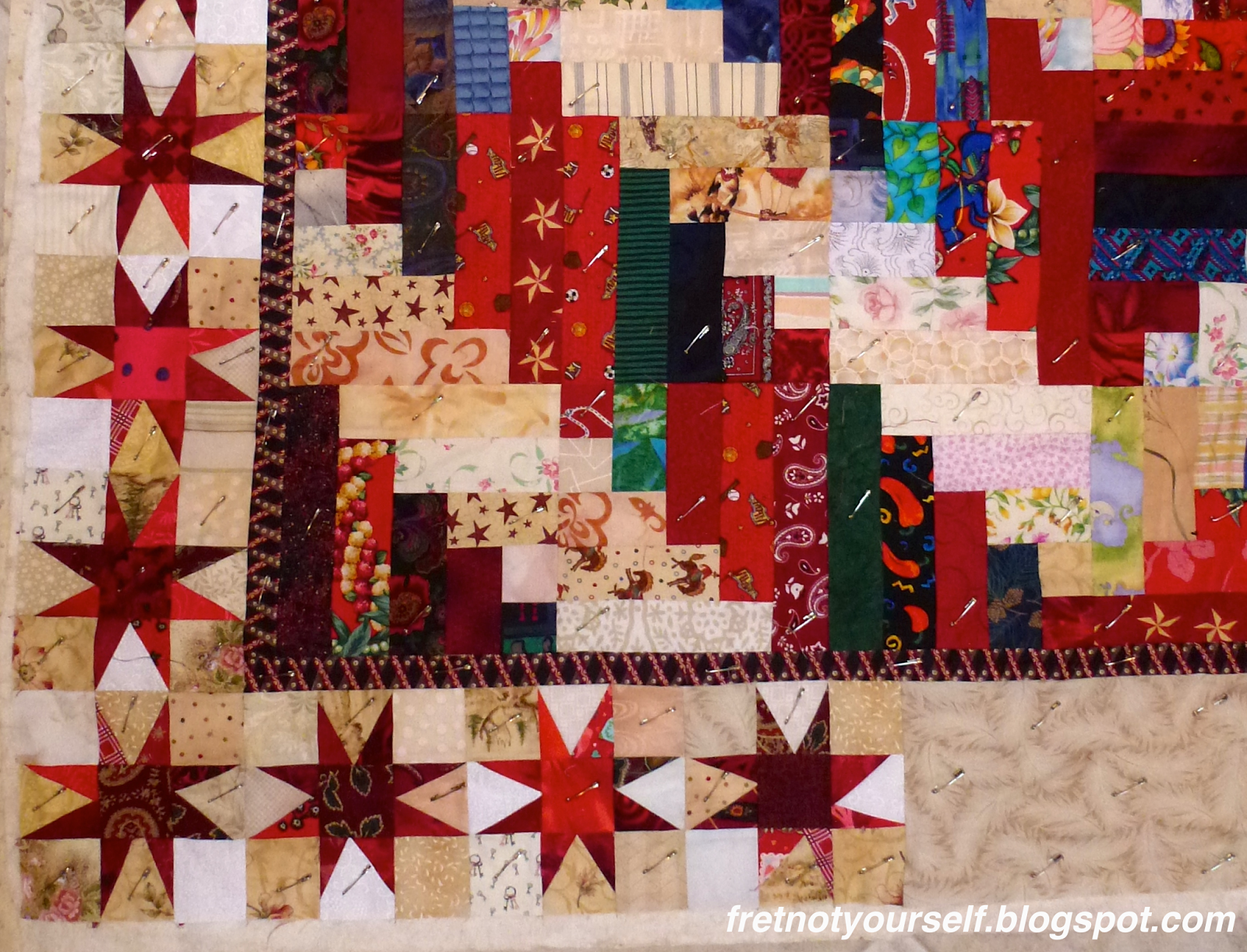Log Cabin variation quilt with border of Liberated Variable Star blocks Log cabin blocks composed of red and cream rectangles for the center. Variable Star blocks of many different red fabrics on cream and white backgrounds for the border.