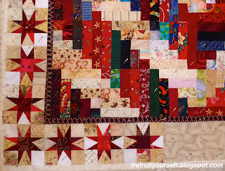 Log cabin blocks composed of red and cream rectangles for the center. Variable Star blocks of many different red fabrics on cream and white backgrounds for the border.