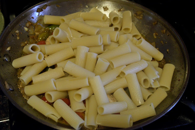 The pasta being added to the skillet on the stove. 