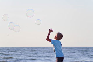 Un verano divertido Chld playing with bubbles in the sea shore