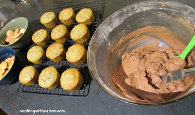 bowl of chocolate frosting next to cooling rack of banana cupcakes