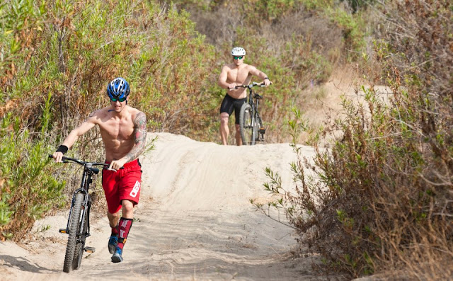 Image of two competitors pushing mountain bikes up a hill in sand during the 2012 CrossFit Games