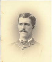 A portrait of a white man with well-combed hair and mustache, wearing a suit.