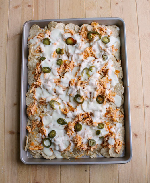 Crunchy tortilla chips topped with buffalo chicken, homemade cheese sauce and your favorite toppings. It's a perfect game day snack! sheet pan of buffalo chicken nachos with white cheese sauce and jalapenos